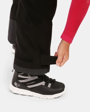Ruka dítěte upravuje suchý zip na nohavici Dětských lyžařských kalhot Kilpi CHARLIE-J černá 110. (3)