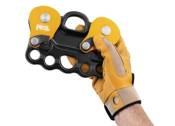 Kladka Petzl Reeve v detailním záběru, držená v ruce s rukavicí na bílém pozadí. (3)